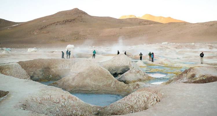 Visitors walk among steaming geysers and mineral pools on high-altitude plain