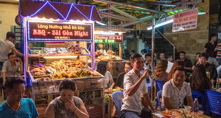Scène de street food avec des gens qui dînent et des stands de nourriture la nuit.