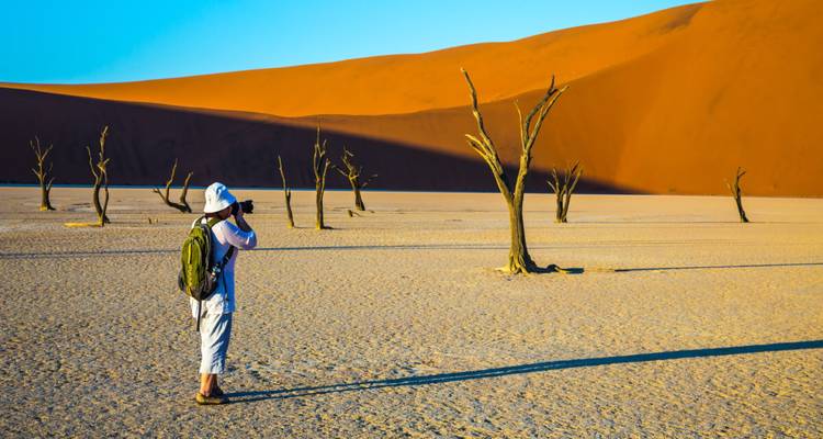 Le photographe se tient à Dead Vlei en prenant des photos des acacia-giraffes aux formes épurées devant les dunes oranges massives.