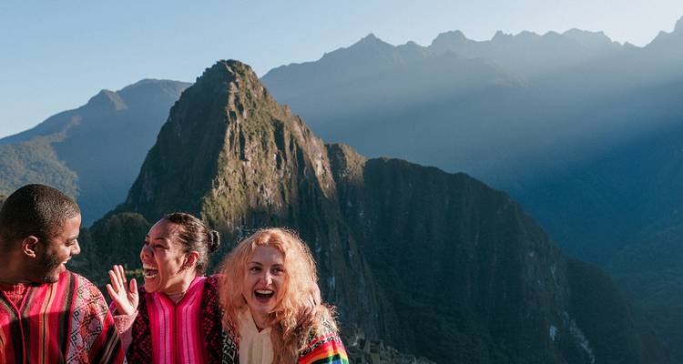Friends wearing colourful ponchos laugh together with the iconic peak of Machu Picchu behind them.