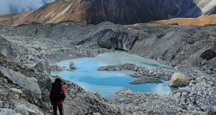 Hiker looking at glacial lake with mountains in the background.