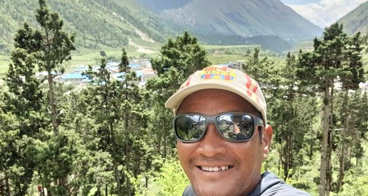 Selfie einer Person mit Sonnenbrille in einem bewaldeten Berggebiet.