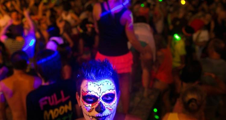 Persoon met gezichtsbeschildering en masker op een levendig nachtfeest.