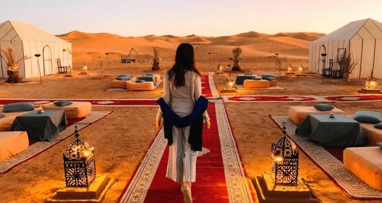 Een vrouw die loopt richting een prachtig opgezet woestijnkamp bij zonsondergang.