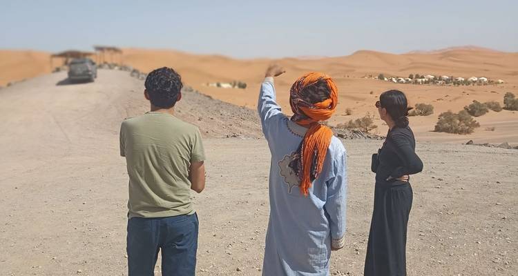 Eine kleine Gruppe von Menschen in traditioneller Kleidung, die ein Wüstenlager in der Ferne betrachtet.