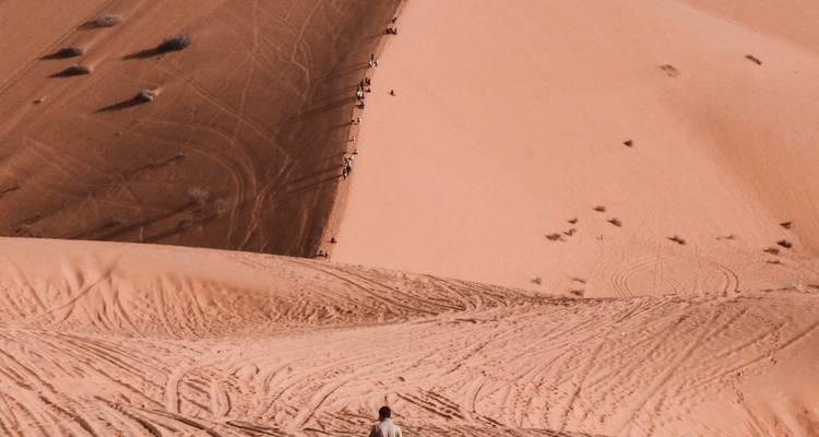 Person, die auf großen Wüstendünen unter einem blauen Himmel geht.