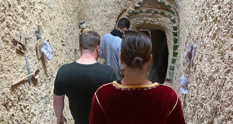 Menschen erkunden einen schmalen, rustikalen tunnelartigen Innenraum.