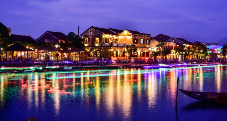 Bunte leuchtende Boote auf einem Fluss bei Nacht in einer lebendigen Stadt.