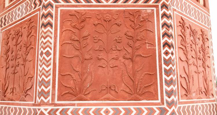 Rote Sandsteinwand mit floralen Verzierungen.