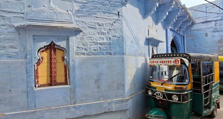 A narrow blue-painted alley with an auto-rickshaw parked beside an ornate window in a historic Indian neighbourhood.