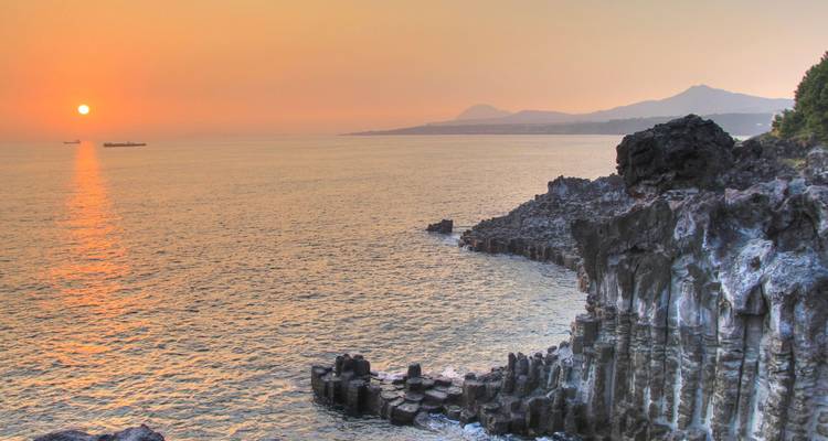 Coucher de soleil sur une côte volcanique accidentée avec des falaises de basalte colonnade et des montagnes lointaines.