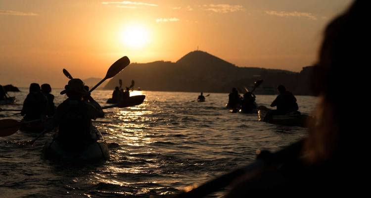 Kayakistes pagayant au coucher du soleil avec des montagnes en arrière-plan.
