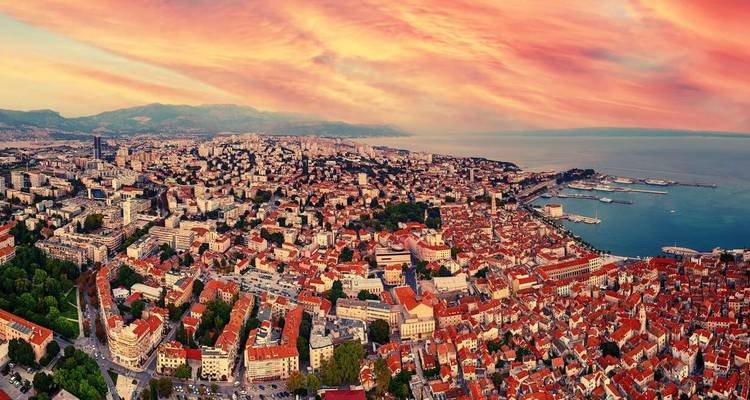 Vue aérienne d'une ville côtière avec des toits rouges et un ciel de coucher de soleil éclatant.