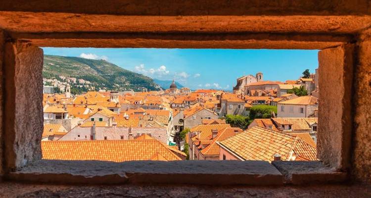 Vue à travers un encadrement de fenêtre en pierre d'une ville aux toits de terre cuite.