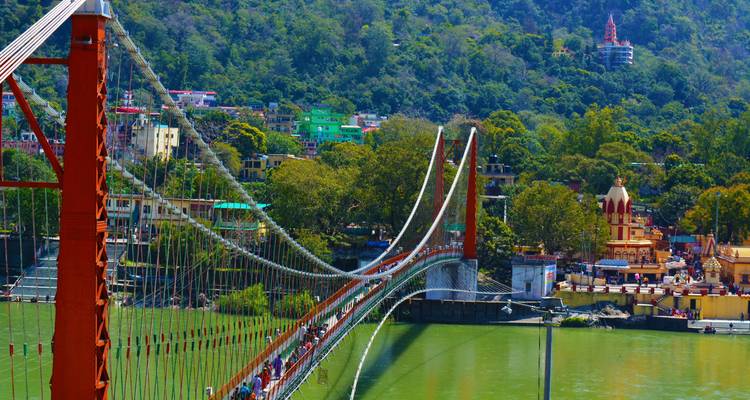 Malerische Aussicht auf eine Hängebrücke über einem Fluss mit Gebäuden im Hintergrund.