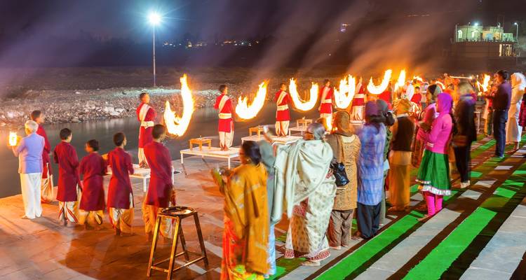 Abendzeremonie mit Flammen und einer Menschenmenge an einem Fluss.