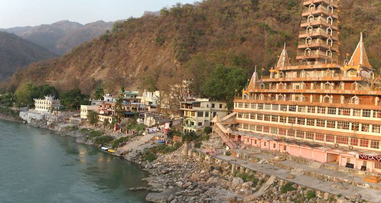 Ein großer mehrstöckiger Tempel neben einem Fluss mit Bergen im Hintergrund.
