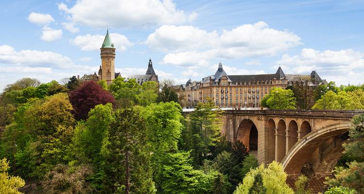 Le pont Adolphe du Luxembourg et le bâtiment bancaire aux tourelles s'élèvent au-dessus d'une verdure printanière dense.