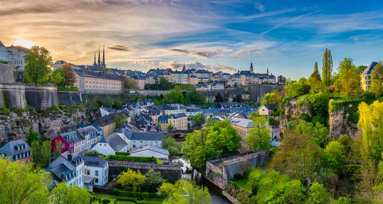 Vue panoramique du coucher de soleil sur la Ville de Luxembourg avec falaises, maisons colorées et ciel dramatique.