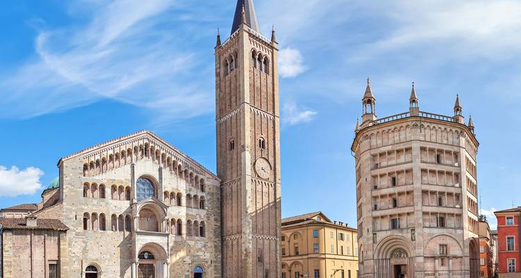 La Catedral de Parma de estilo románico y el Baptisterio octogonal se alzan contra un cielo azul brillante.