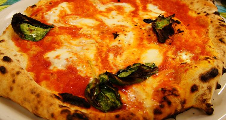 Gros plan sur une pizza margherita classique avec mozzarella fondue, croûte carbonisée et feuilles de basilic.