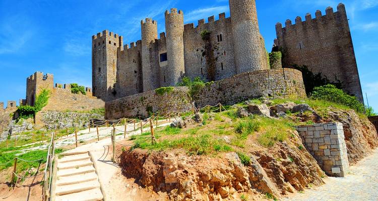 Muros de piedra medieval y torres del Castillo de Óbidos elevándose sobre un camino rocoso en la colina