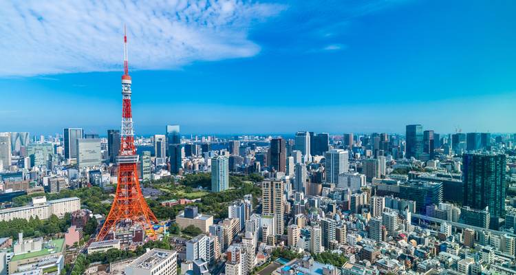 Paysage urbain avec une tour rouge et blanche proéminente, de nombreux gratte-ciel et un ciel bleu dégagé.