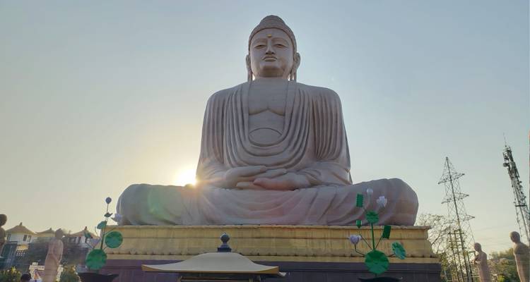 Large seated Buddha statue with the sun setting directly behind, creating a warm halo effect.