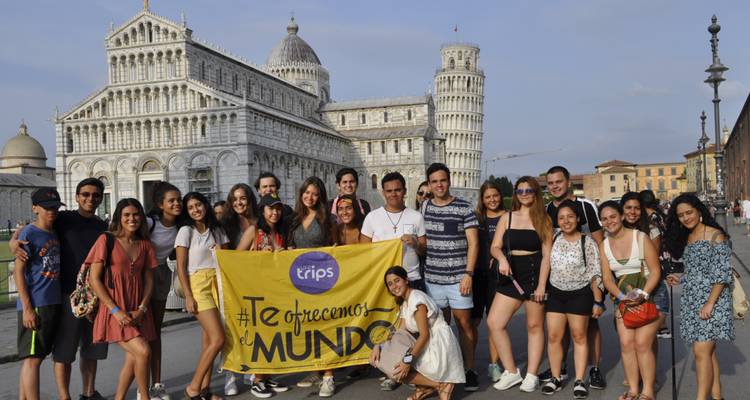 Large group posing with a banner in front of Pisa Cathedral and Leaning Tower.