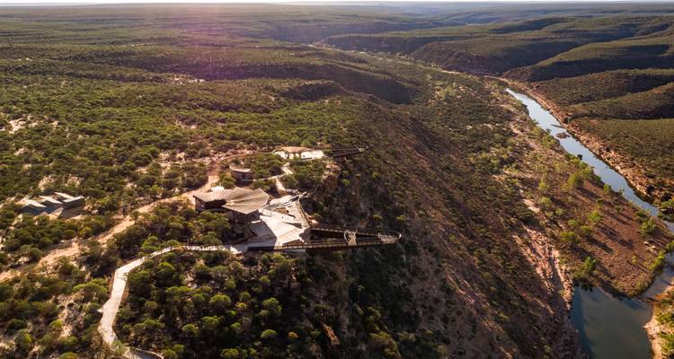 Vue aérienne d'un spectaculaire canyon fluvial avec une passerelle en porte-à-faux et des terres broussailleuses s'étendant jusqu'à l'horizon.