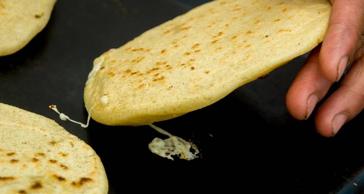 Hand die een tortilla-achtig voedingsmiddel met kaas optilt.