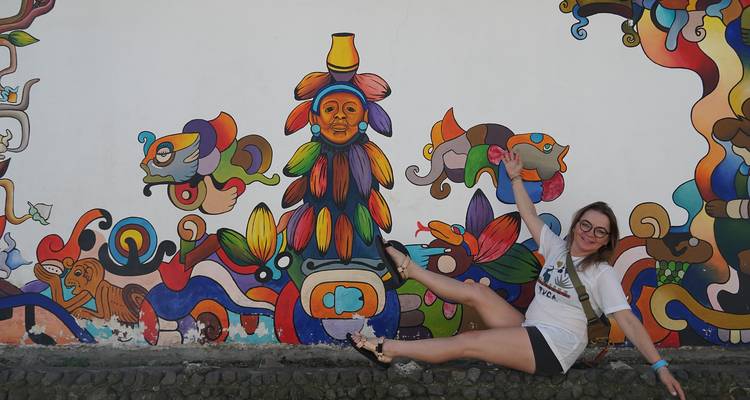 Persoon poseert voor kleurrijke muurschildering met speelse uitdrukking.