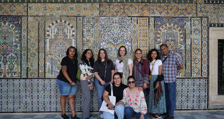 Groupe de personnes debout devant un mur de mosaïque complexe.