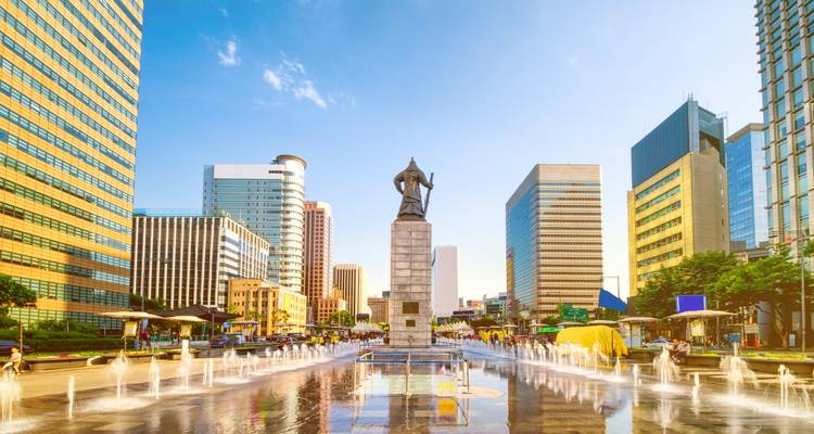 City square with fountains and a statue at sunrise.