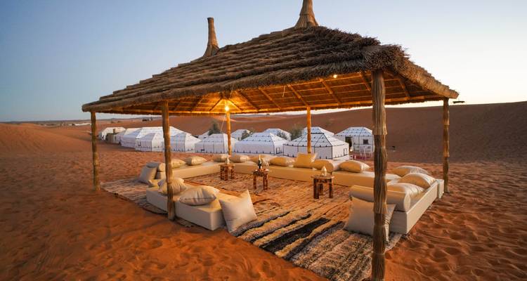 Wüstencamp mit einem Sitzbereich und weißen Zelten im Hintergrund.