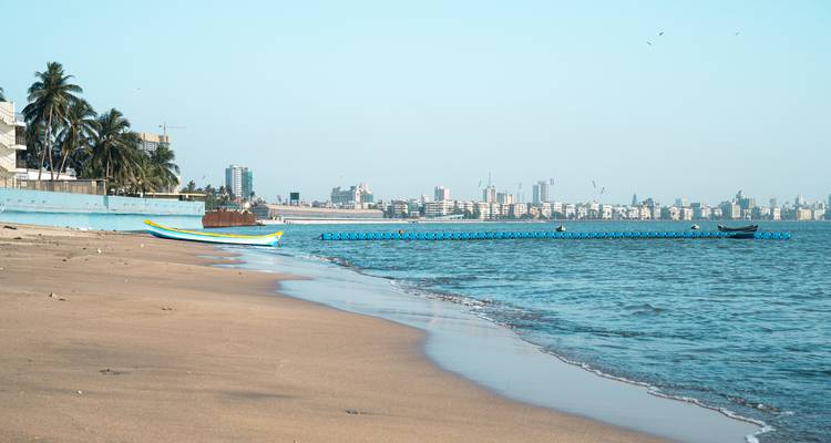 Ruhiger Sandstrand in Mumbai mit Skyline und kleinen Fischerbooten.