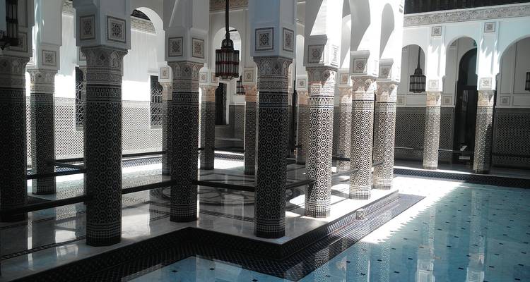 Zonbeschenen binnenplaats met sierlijke zuilen, ingewikkelde zellij-tegels en een ondiepe reflectievijver in Marokko.