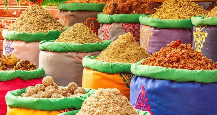 Des sacs vibrants d'épices et d'herbes marocaines dans un souk animé arrangés dans un arc-en-ciel de couleurs.