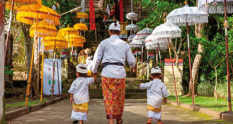 Un homme et deux enfants en tenue traditionnelle balinaise marchant vers un temple.