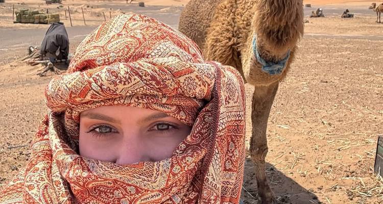 Gros plan d'une femme en tenue du désert avec un chameau en arrière-plan.