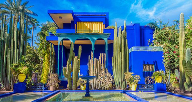 Un bâtiment d'un bleu saisissant entouré de cactus et de jardins luxuriants.