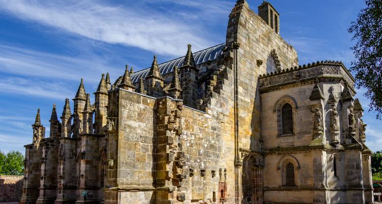 Stone Rosslyn Chapel displays intricate buttresses beneath bright blue Scottish sky