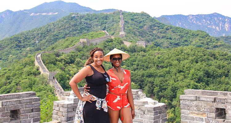 Zwei Personen posieren an der Chinesischen Mauer mit üppigen Hügeln im Hintergrund.