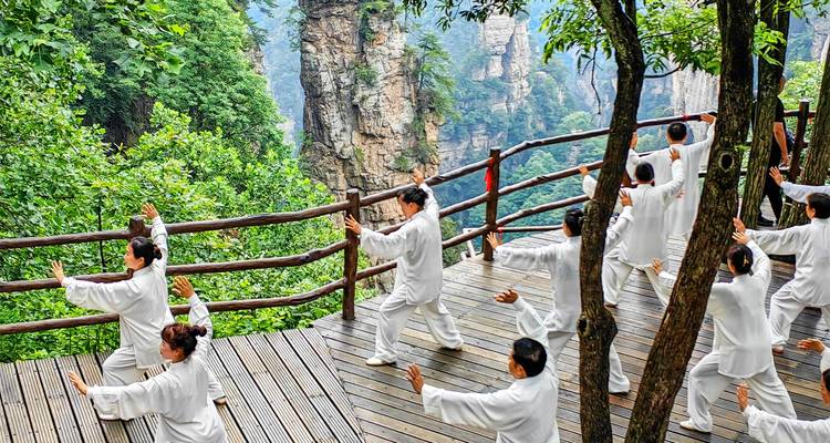 Beoefenaars voeren Tai Chi uit op een houten uitkijkplatform met uitzicht op dramatische zandstenen pilaren in mistige bergen.