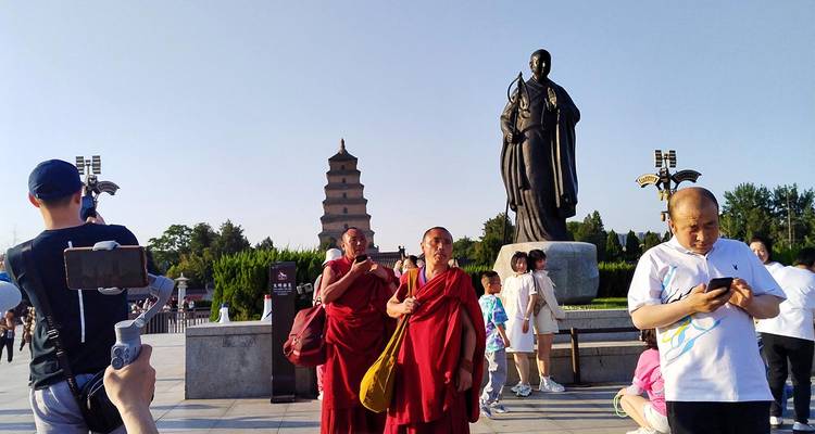 Monniken en toeristen staan bij het standbeeld van Xuanzang met de Grote Wilde Gans Pagode op de achtergrond op een heldere dag.