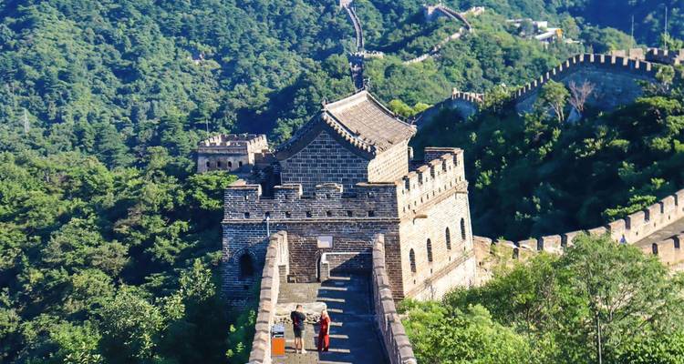 Scenic section of the Great Wall of China snaking across lush green mountains with a stone watchtower in the foreground.