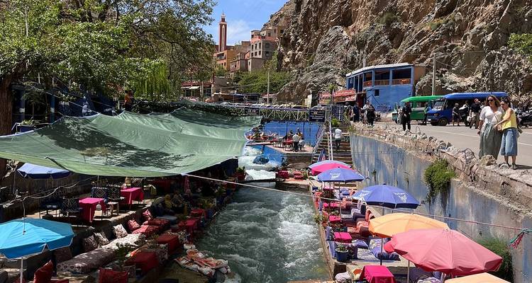 Plateformes d'assise colorées au bord de la rivière avec tapis et parasols près d'un torrent rapide dans un village de montagne avec un grand minaret.