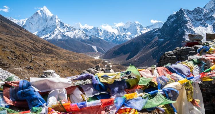 Schneebedeckte Berglandschaft mit bunten Gebetsfahnen im Vordergrund.