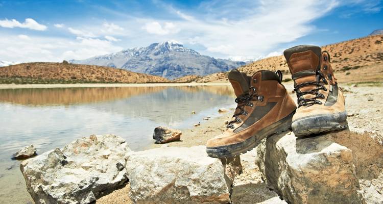 Ein Paar Wanderstiefel auf Felsen neben einem ruhigen See mit einem Berg im Hintergrund.