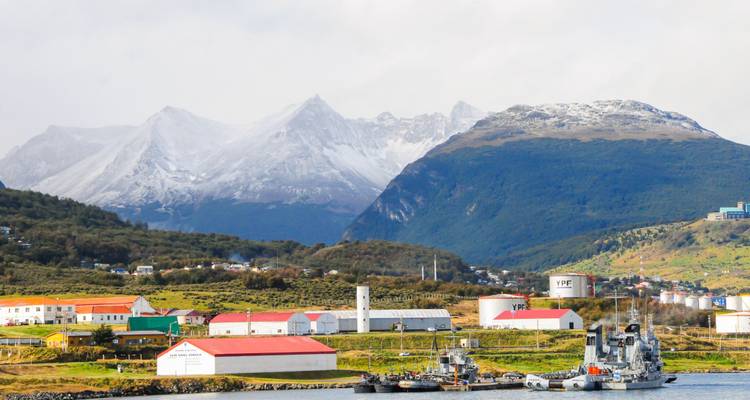 Ville au bord de l'eau avec des montagnes enneigées en arrière-plan.